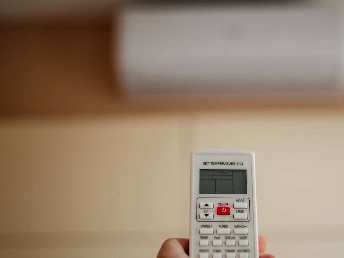 Pessoa aponta controle remoto para unidade de ar-condicionado split na parede